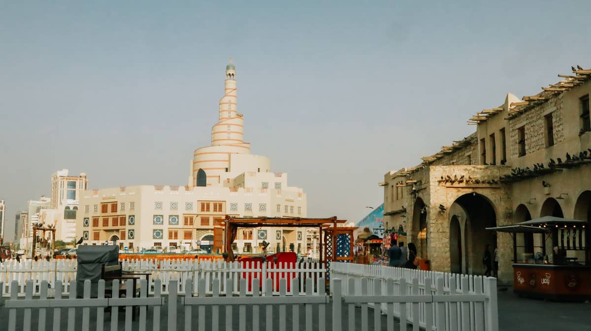 Traditionelle katarische Gebäude und das spiralförmige Minarett des Islamischen Kulturzentrums Fanar, mit einem lebhaften Platz im Vordergrund in Doha.