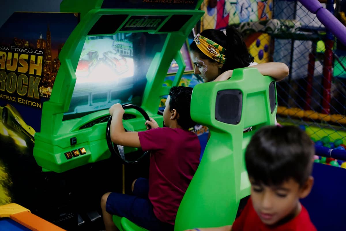 Kinder spielen ein Arcade-Fahrspiel in einem farbenfrohen Indoor-Spielbereich mit Netzwänden und lebendiger Dekoration.