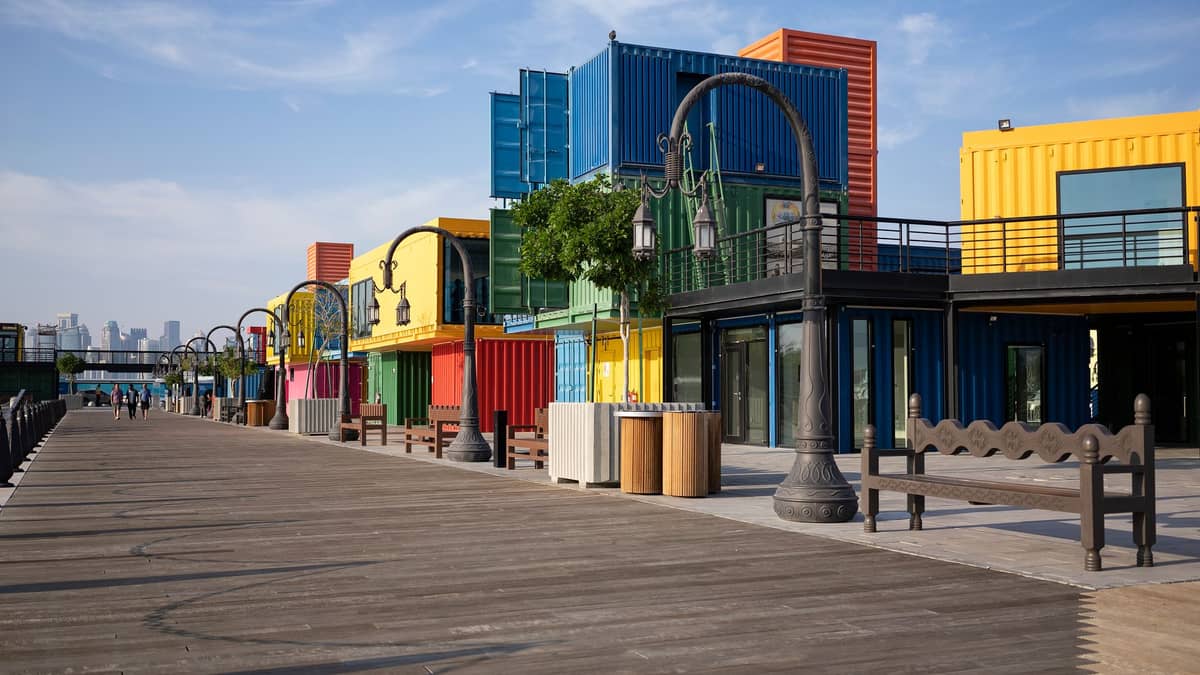 Bunte Frachtcontainer-Gebäude entlang einer Promenade unter blauem Himmel, in Anlehnung an das einzigartige containerbasierte Design des Stadium 974.