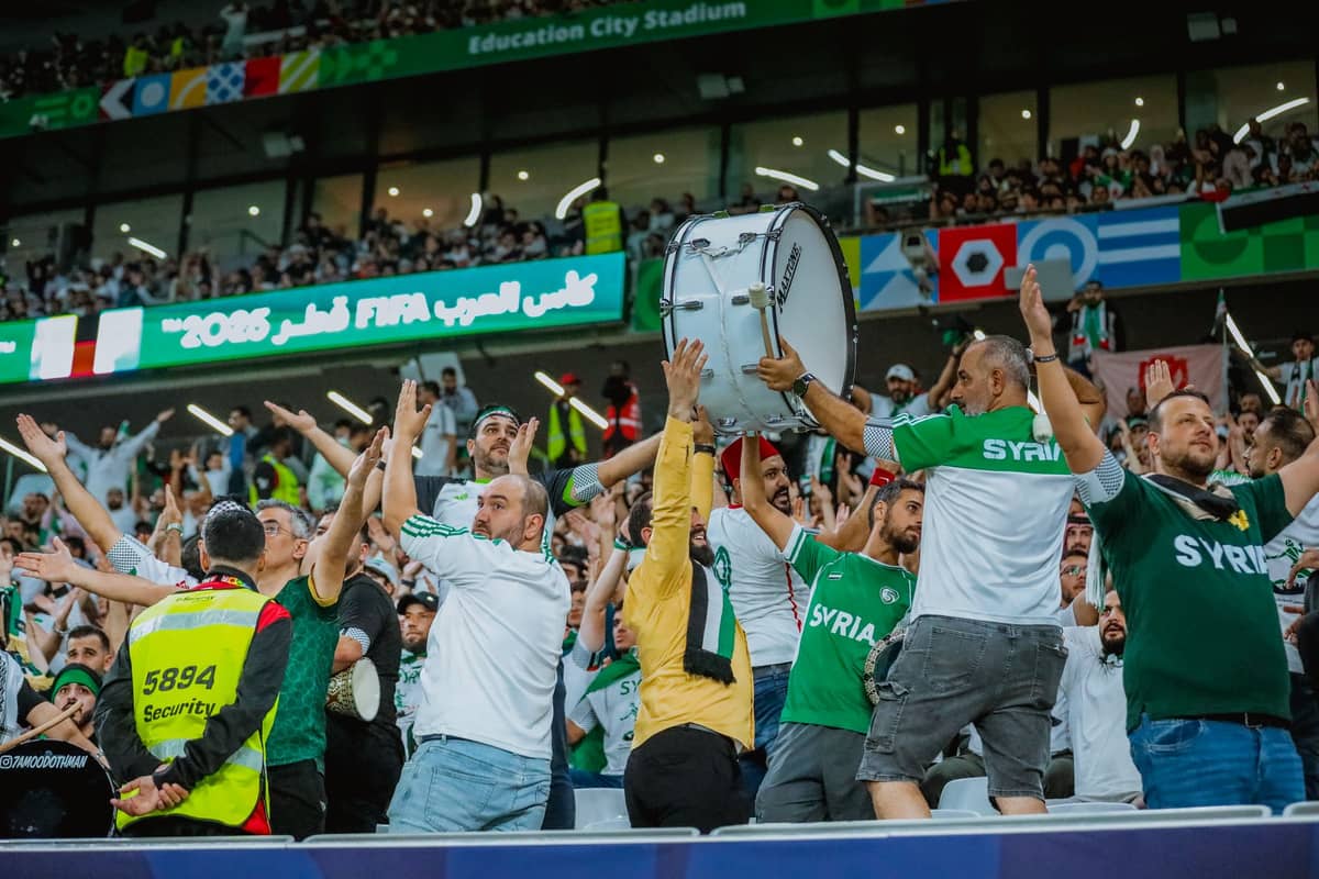 Begeisterte Fußballfans in grünen Syrientrikots jubeln und feiern im Education City Stadium in Doha während einer FIFA-Veranstaltung.
