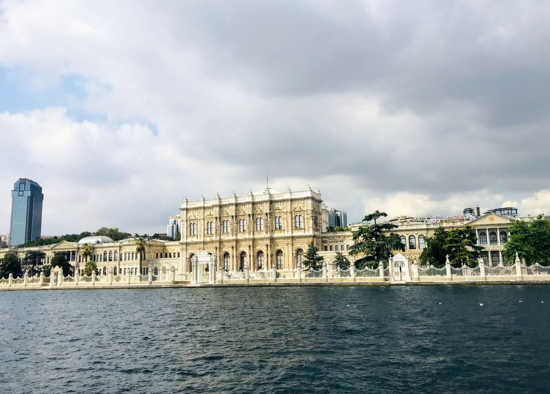 Vista panoramica della facciata sul mare del Palazzo di Dolmabahçe che si estende lungo il Bosforo, incorniciata da un cielo nuvoloso e dall'acqua scintillante, che mette in risalto la scala e la posizione del palazzo.