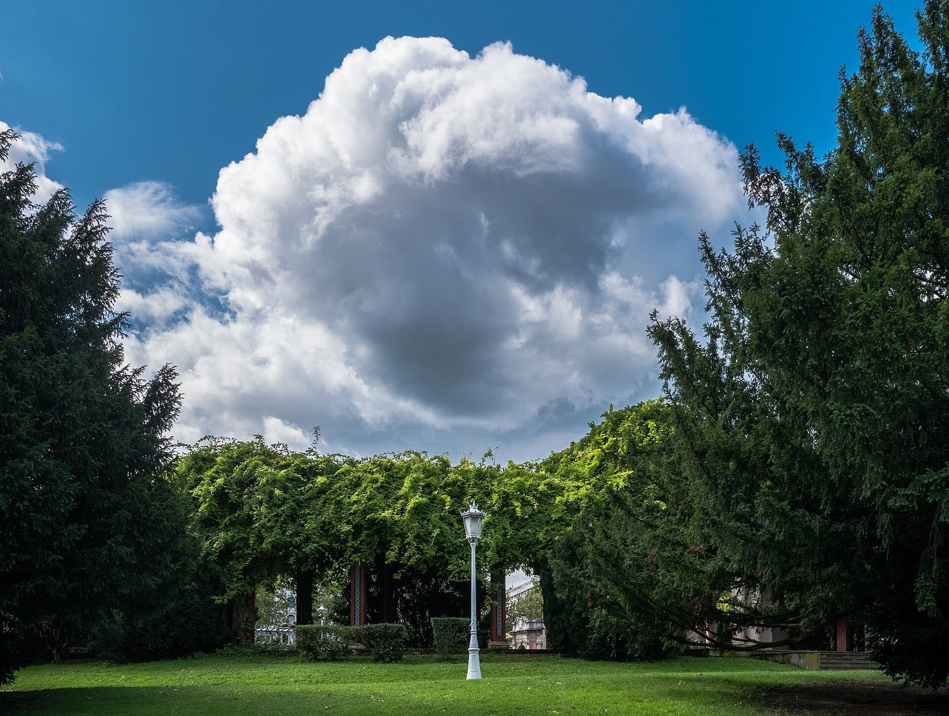 Lush green lawns, mature trees, and a vintage white lamp post at Parque de Doña Casilda Iturrizar under a dramatic cloudy sky.