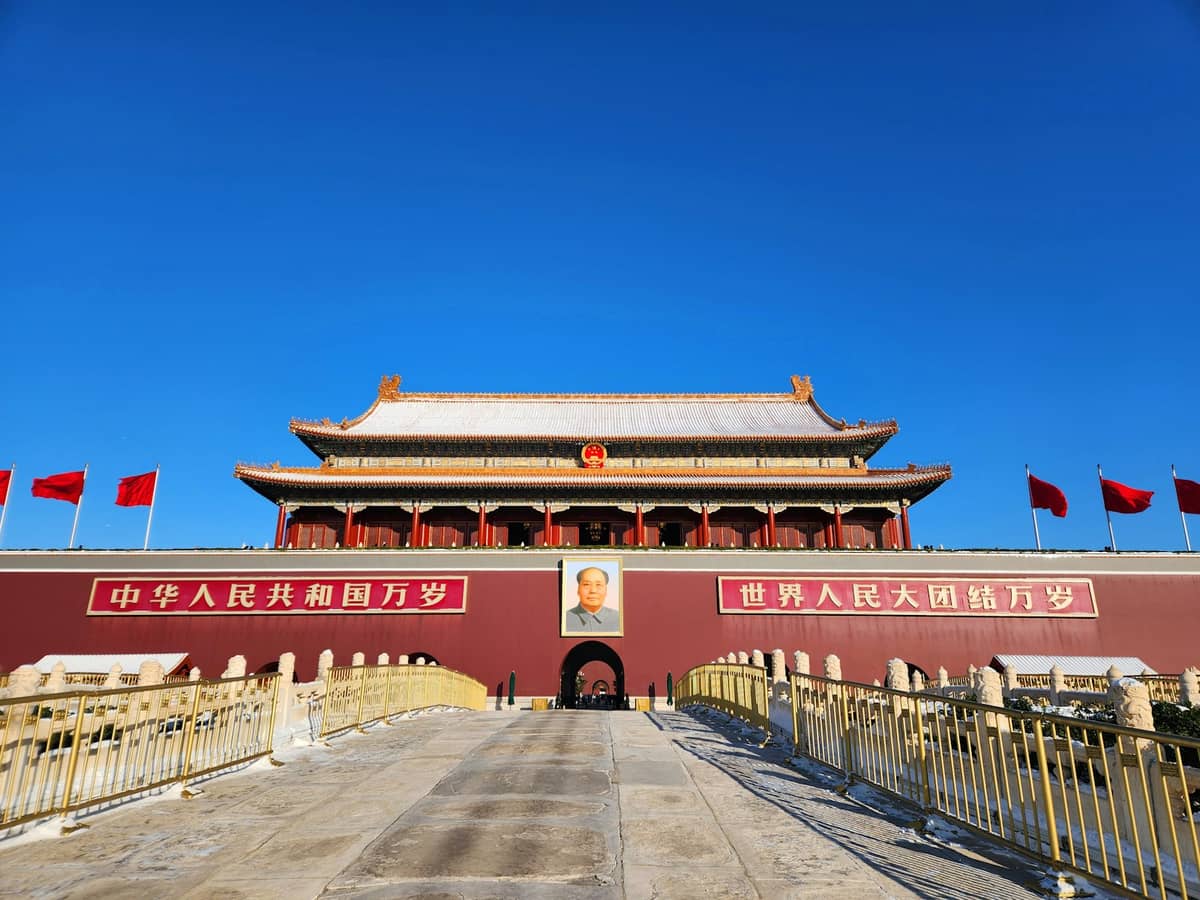 Das Tiananmen-Tor mit leuchtend roten Mauern, roten Fahnen und einem Porträt von Mao Zedong unter strahlendem blauem Himmel im Dongcheng District, Peking.