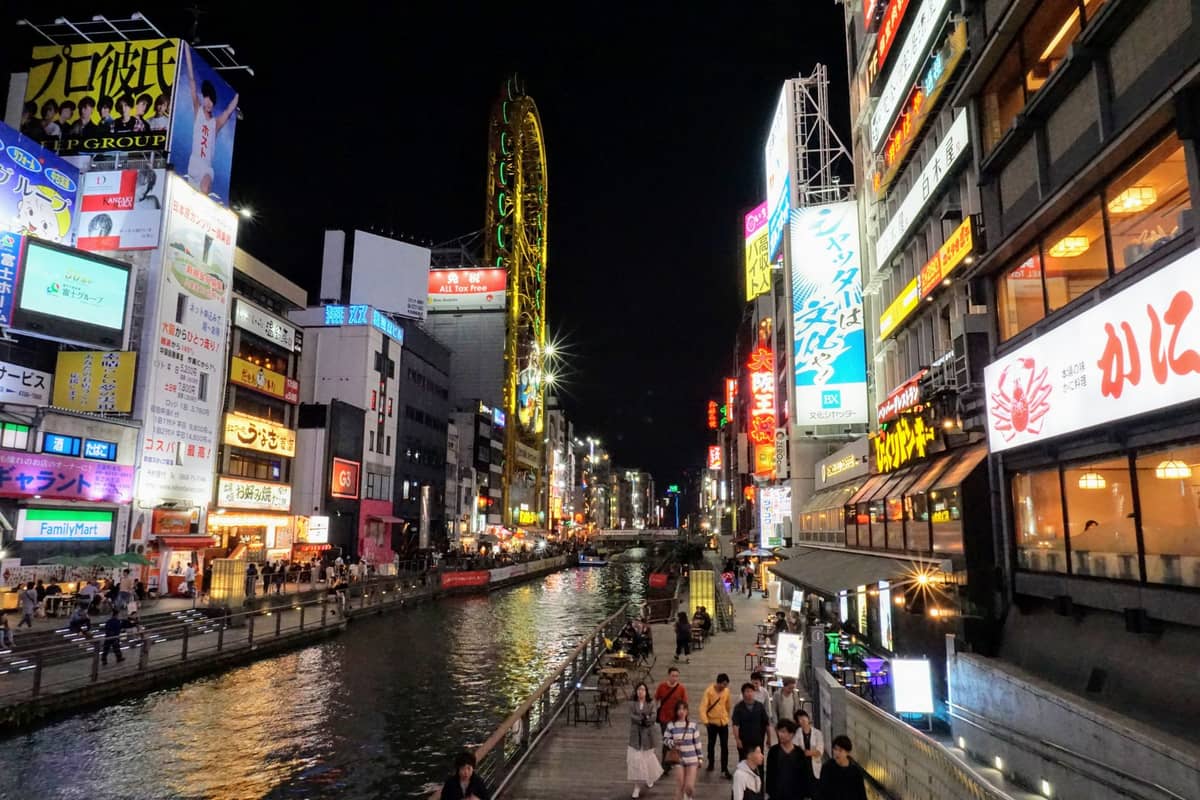 Night view of Dotonbori canal in Osaka with colorful neon signs, busy walkways, and reflections on the water, capturing the lively atmosphere.