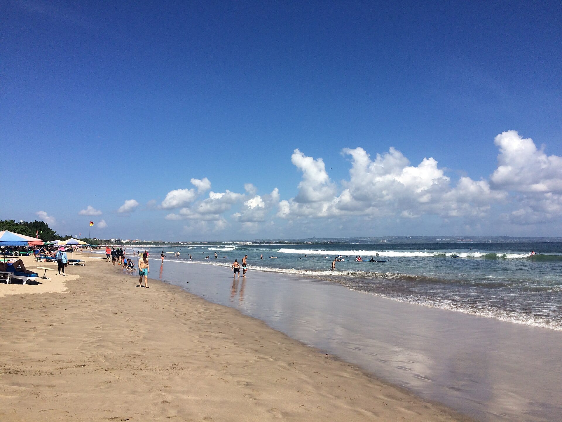 La vasta sabbia bianca della spiaggia Double Six a Seminyak, con ombrelloni e onde dolci che lambiscono la riva.