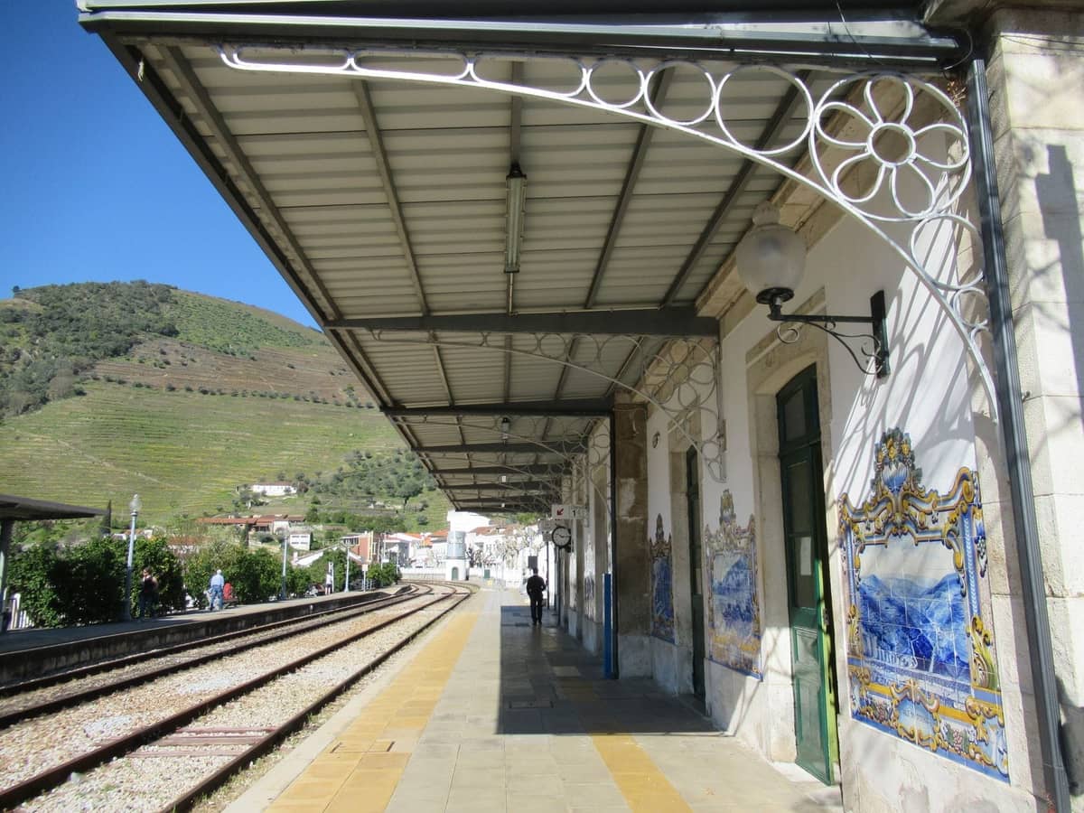 Widok na peron stacji kolejowej Pinhão ozdobiony panelami z azulejos przedstawiającymi wiejskie sceny z Doliny Douro, ze wzgórzami w tle.
