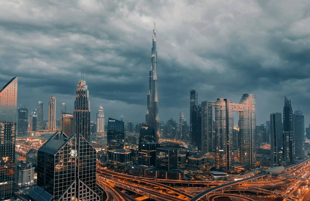 Skyline von Downtown Dubai mit dem Burj Khalifa im Zentrum und umliegenden Hochhäusern, aus der Vogelperspektive mit bewölktem Himmel und großen Straßen im Vordergrund.