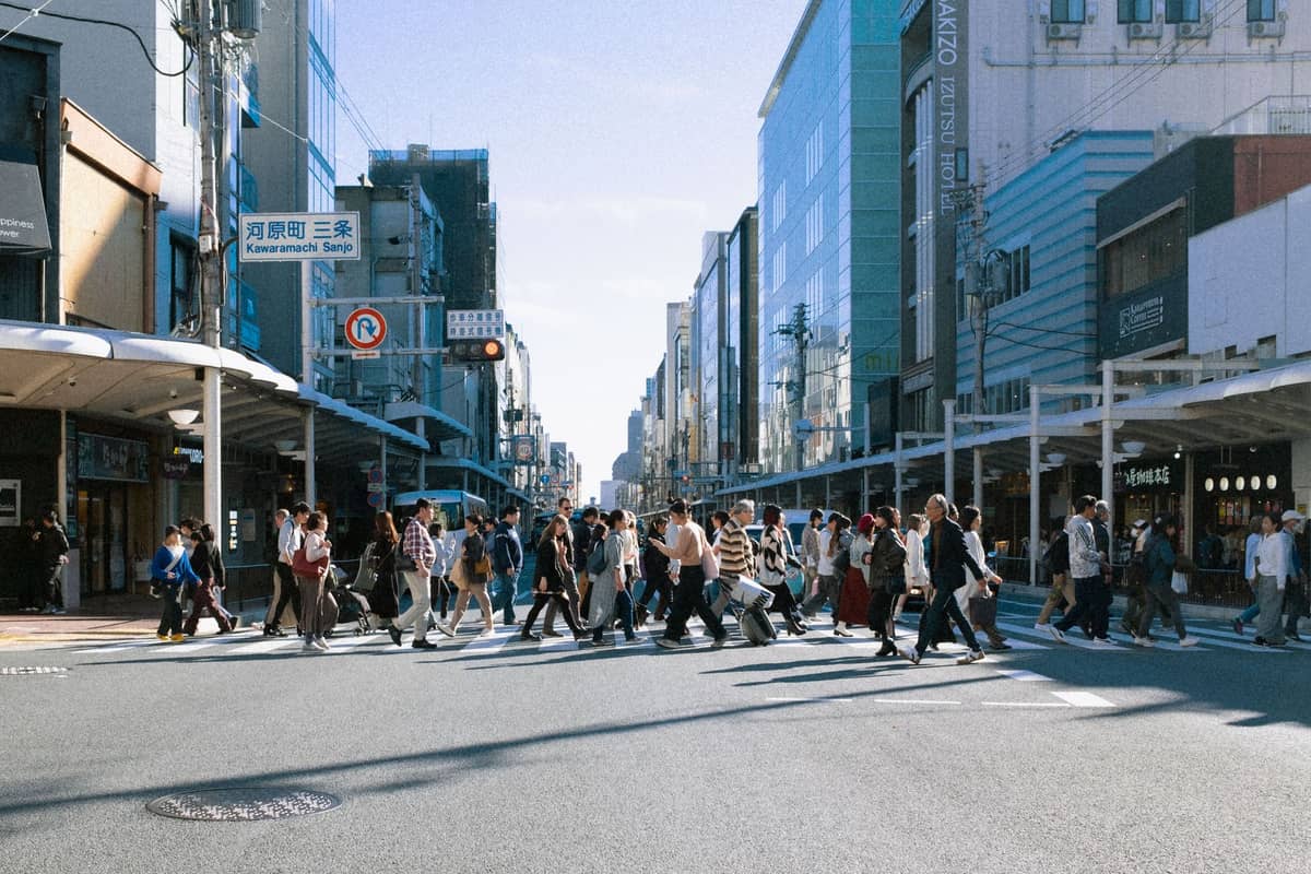 Crowds of people crossing the street at the busy Kawaramachi and Shijo intersection in downtown Kyoto, with department stores and arcades lining both sides.