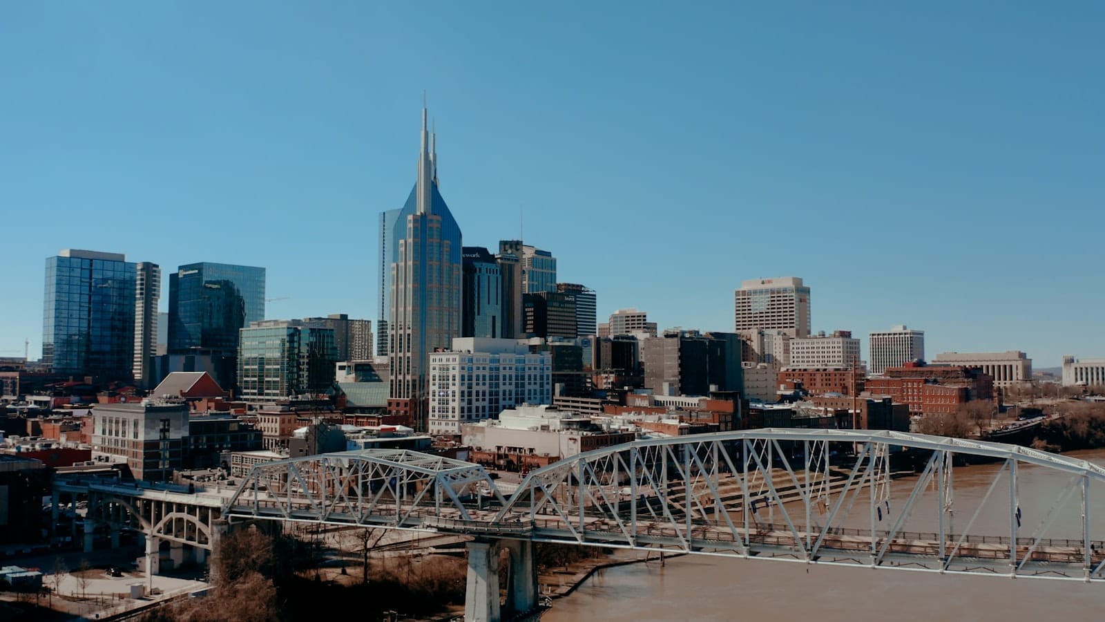 Vista panorámica del horizonte del centro de Nashville con rascacielos modernos, edificios históricos y un puente sobre el río Cumberland en un día soleado y despejado.