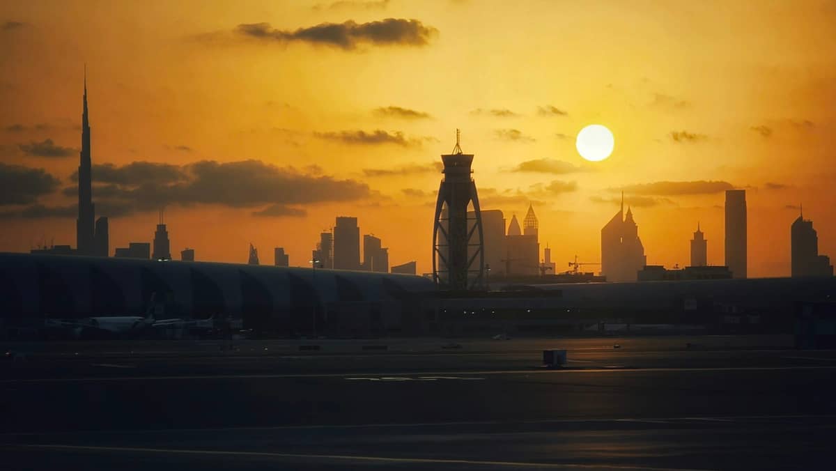 Der Dubai International Airport bei Sonnenuntergang mit dem Kontrollturm und der Skyline Dubais, einschließlich des Burj Khalifa, im Hintergrund.