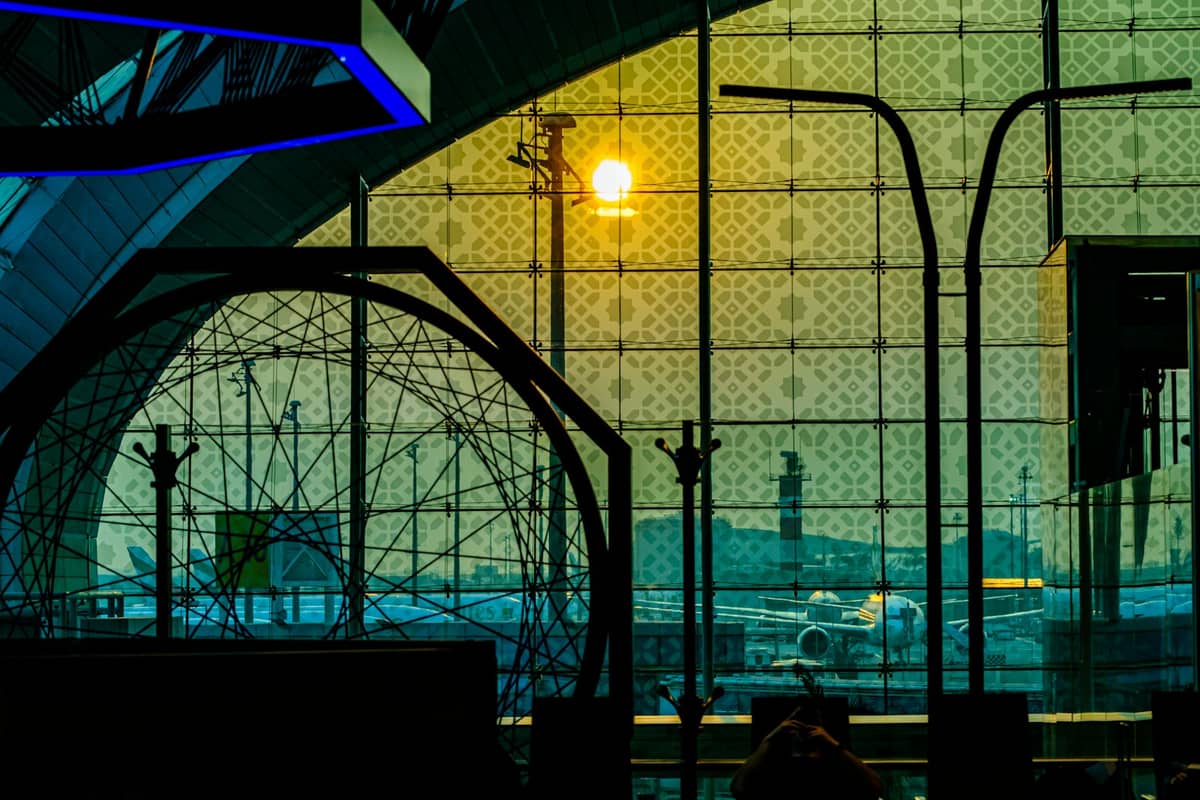 Innenansicht des Terminals des Dubai International Airport mit gemustertem Glas, draußen sichtbaren Flugzeugen und warmem Abendsonnenlicht, das hereinstrahlt.