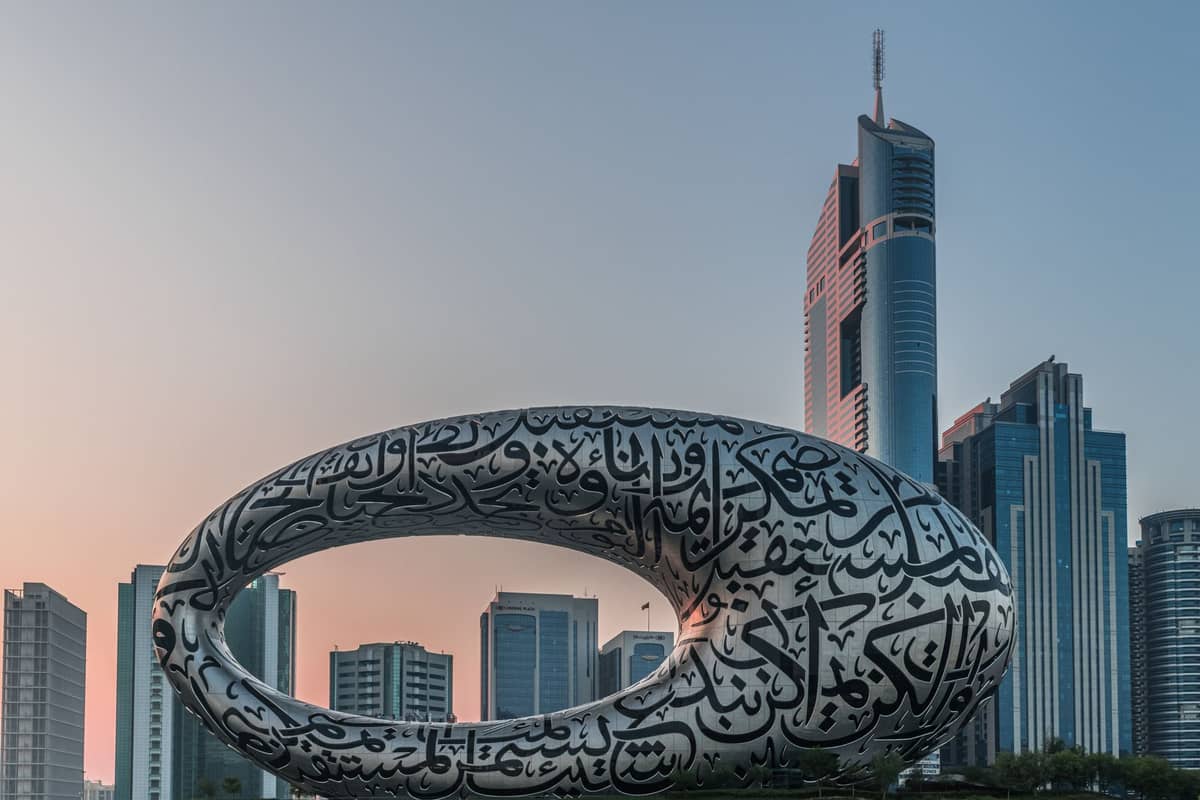 Das Museum of the Future in Dubai, ein torusförmiges Gebäude mit arabischer Kalligrafie, umgeben von Wolkenkratzern der Stadt bei Sonnenuntergang.