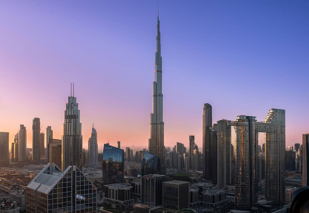 Skyline der Innenstadt von Dubai in der Abenddämmerung mit dem Burj Khalifa und mehreren anderen Supertall-Wolkenkratzern vor einem blau-violetten Verlaufshimmel.