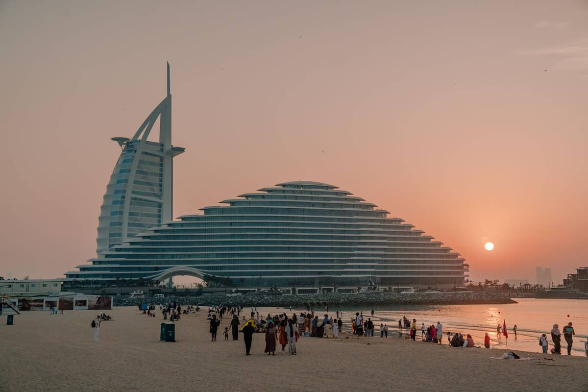 Menschenmengen genießen den öffentlichen Sandstrand bei Sonnenuntergang mit dem Hotel Burj Al Arab im Hintergrund in Dubai.