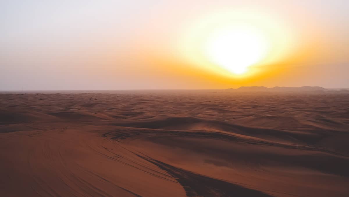 Weite Landschaftsansicht der Wüstendünen von Dubai bei Sonnenuntergang mit goldenem Himmel und sanften Schatten, die ein Gefühl von Timing und jahreszeitlichem Wandel hervorrufen.