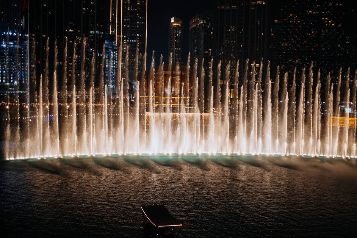 Die Dubai Fountain bei Nacht, mit hohen Wasserstrahlen, die im Lichterglanz vor der Stadtkulisse choreografiert tanzen.