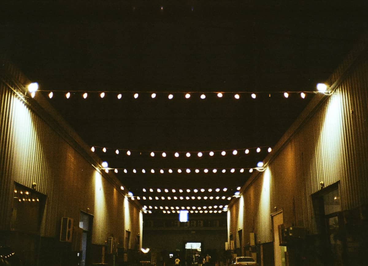 Lichterketten hängen über einer städtischen Gasse, die nachts von Gebäuden im Lagerhausstil gesäumt ist, und erinnern an Dubais kreative Kunstbezirke wie die Alserkal Avenue.