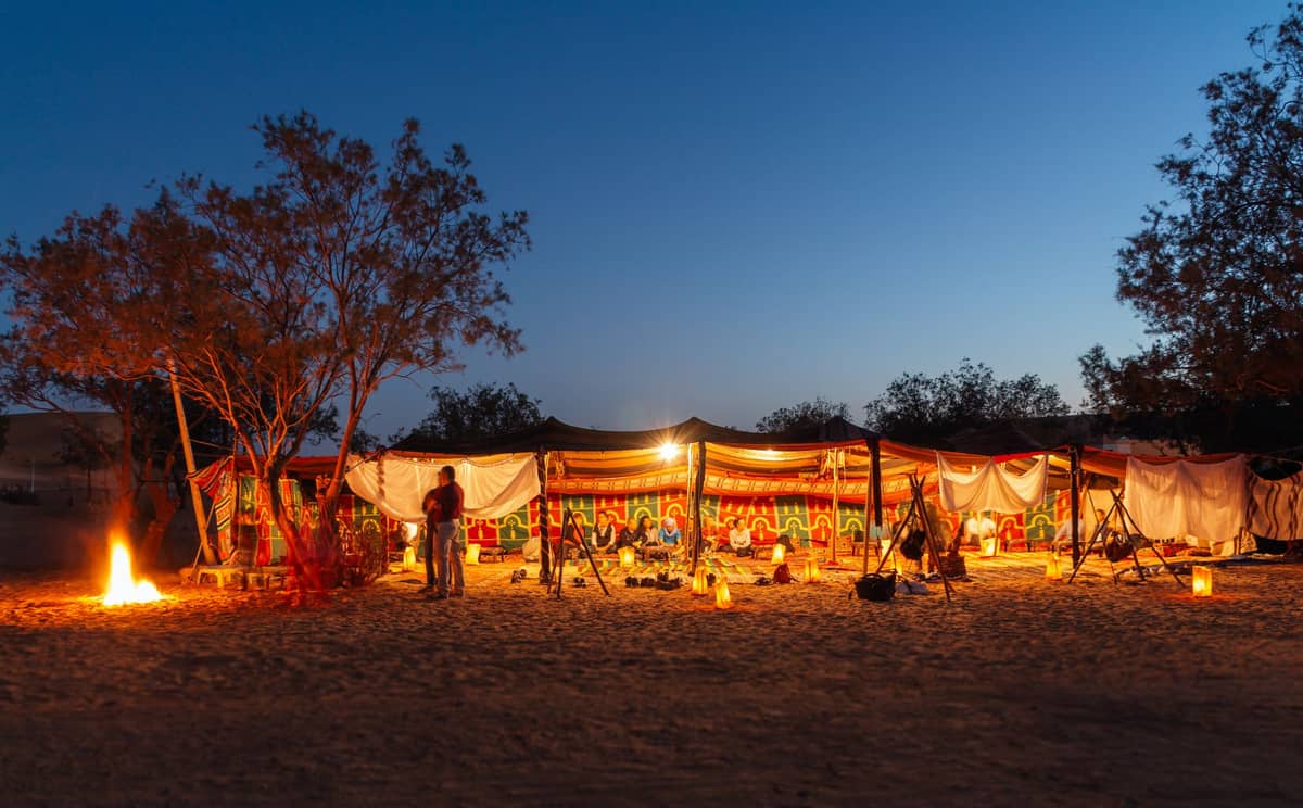 Buntes Wüstenlager in der Abenddämmerung mit Menschen, Laternen und einem Lagerfeuer in der Wüste von Dubai.