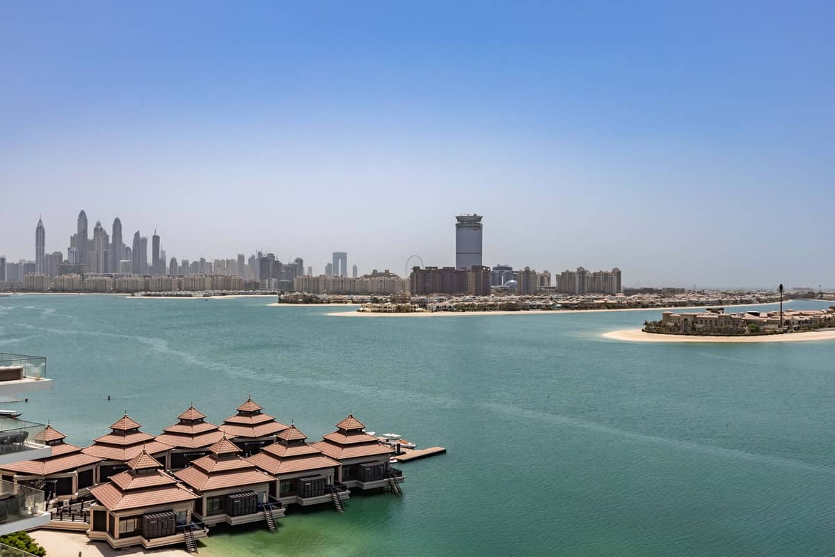 Überwasser-Villen auf Palm Jumeirah mit der Skyline von Dubai Marina und ruhigem blauem Wasser unter klarem Himmel, die Luxus und Abgeschiedenheit vermitteln.