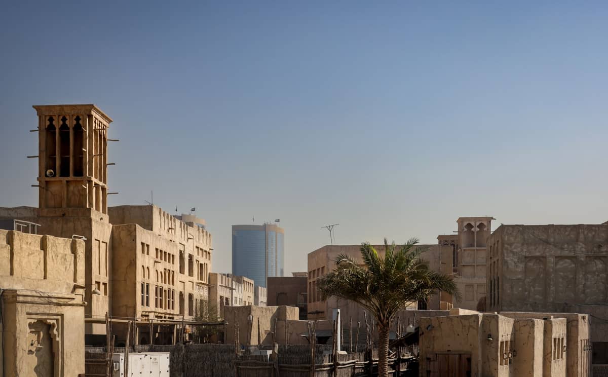 Restaurierte Windturm-Architektur und enge Gassen im historischen Viertel von Dubai, mit traditionellen sandfarbenen Gebäuden und einer Palme unter klarem Himmel.