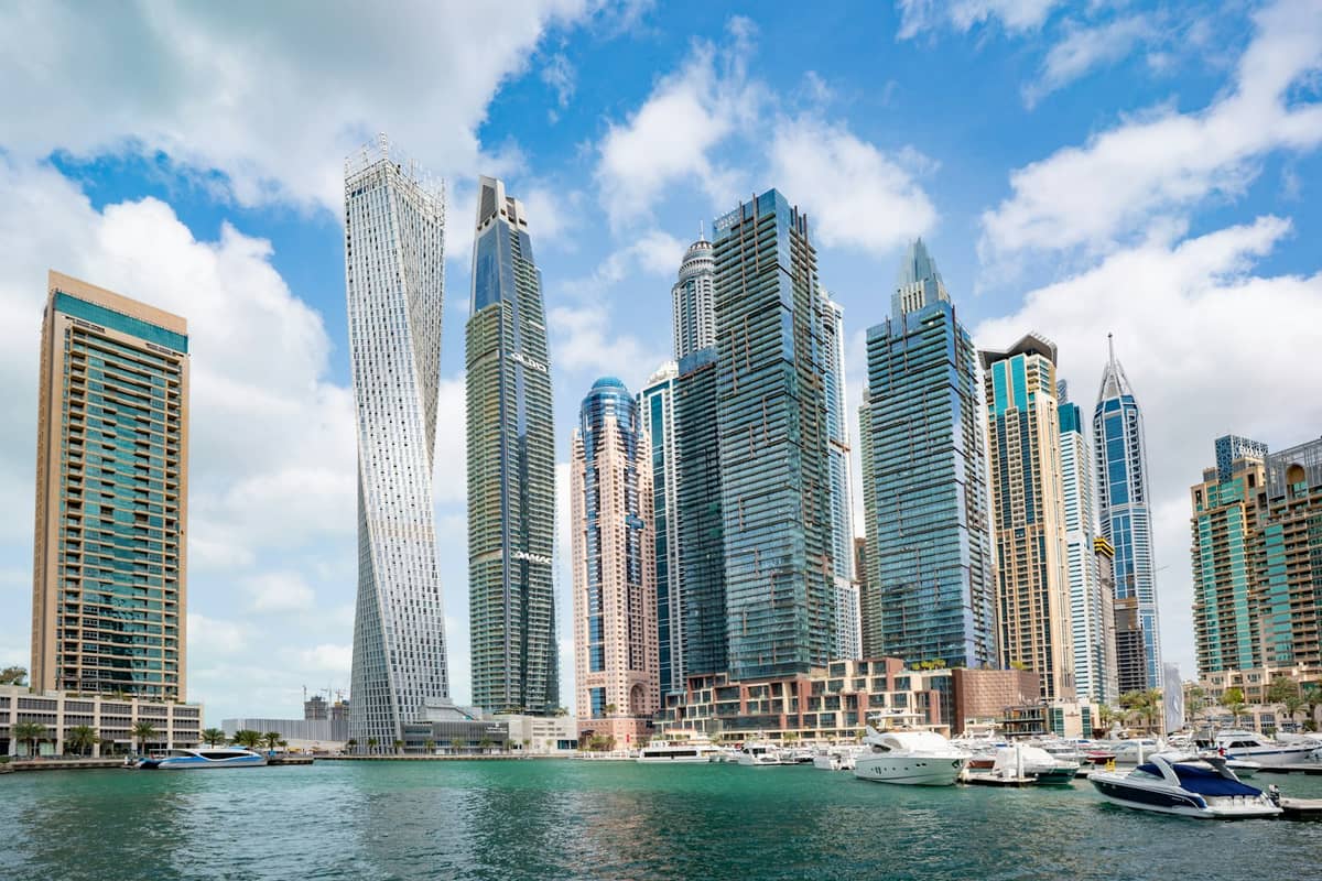 Tagansicht der Dubai Marina mit modernen Hochhäusern und einem Ufer voller Yachten unter blauem Himmel mit einigen Wolken.