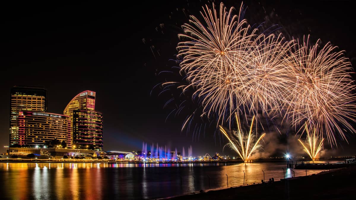 Feuerwerk über dem Dubai Creek in der Nähe prominenter Hotels, mit bunten Lichtern, die sich nachts im Wasser spiegeln.