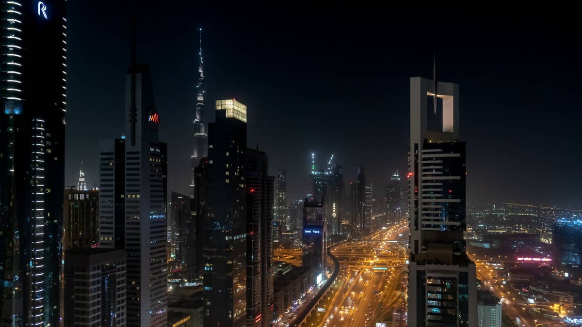 Die Sheikh Zayed Road in Dubai bei Nacht, mit beleuchteten Metroschienen und Wolkenkratzern der Stadt, darunter der Burj Khalifa in der Ferne.