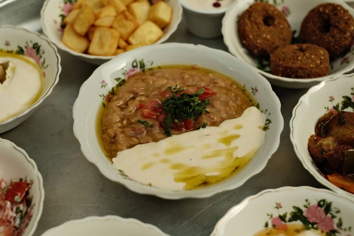 Eine Auswahl an Mezze-Gerichten aus dem Nahen Osten mit Bohnen, Falafel und Kartoffeln, serviert in dekorierten Schalen auf einem Metalltisch.