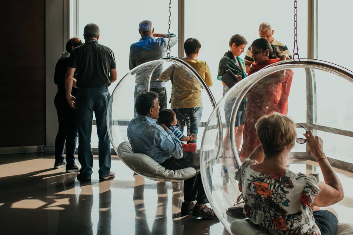 Besucher sitzen in hängenden Bubble-Chairs und stehen an großen Glasfenstern einer Aussichtsplattform mit Blick auf die Stadt.