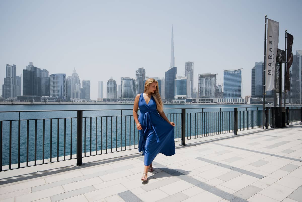 Frau in blauem Kleid auf der Uferpromenade von Dubai, im Hintergrund der Burj Khalifa und die Stadtsilhouette.