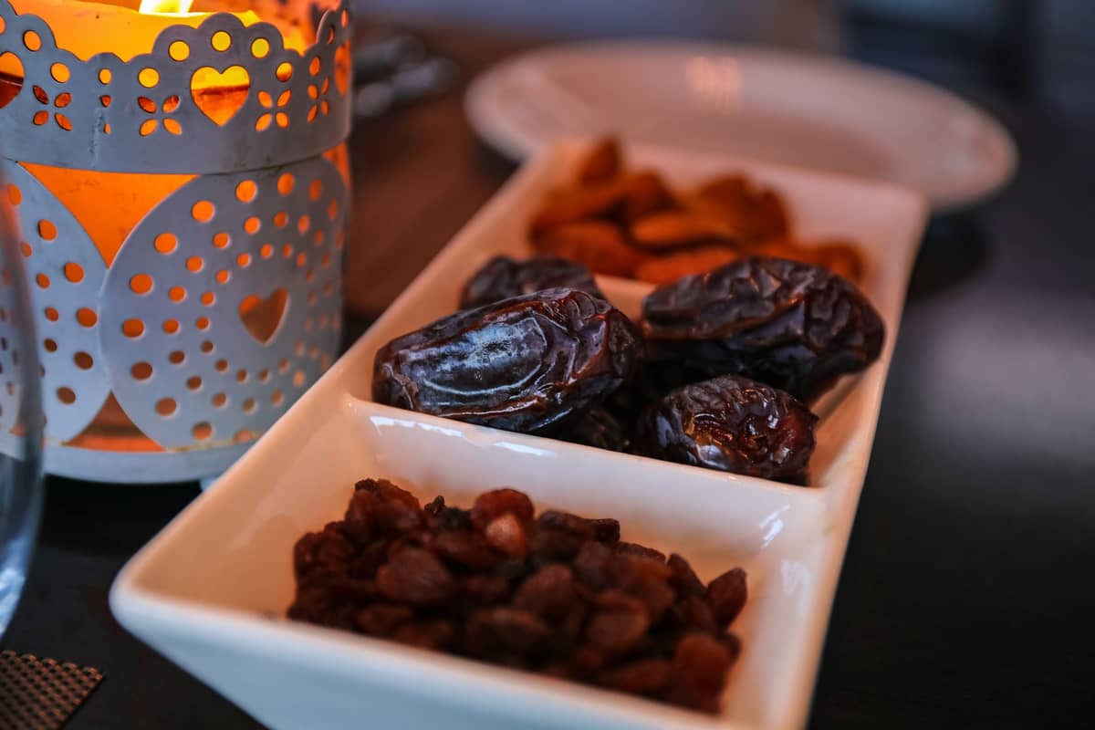 Nahaufnahme eines Tellers mit Datteln und getrocknetem Obst neben einer dekorativen Kerze, die die Iftar-Atmosphäre des Ramadan in Dubai heraufbeschwört.