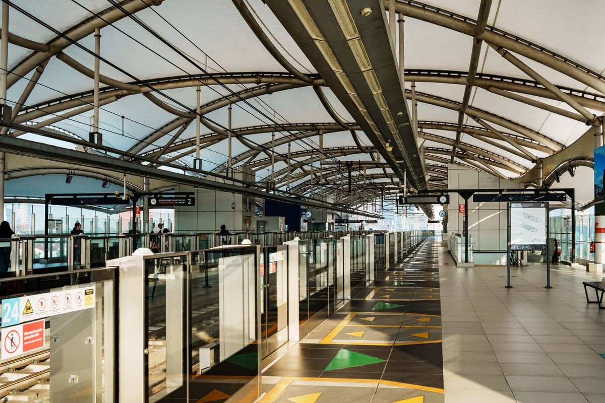 Innenansicht eines Bahnsteigs einer Dubai-Metro-Station mit Glasbarrieren, Richtungsmarkierungen auf dem Boden und moderner Architektur.
