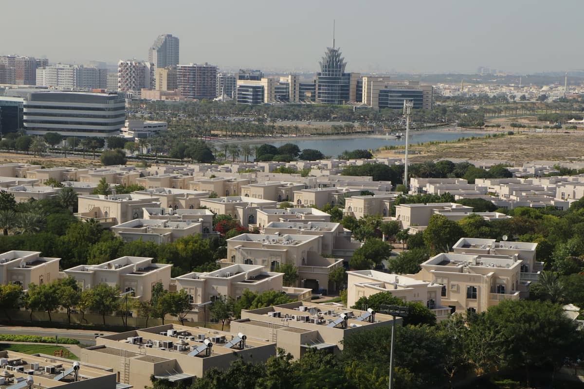 Moderne Stadtlandschaft von Dubai mit einem See, Villen und Bürogebäuden, die tagsüber Wohn- und Verwaltungsbereiche zeigt.