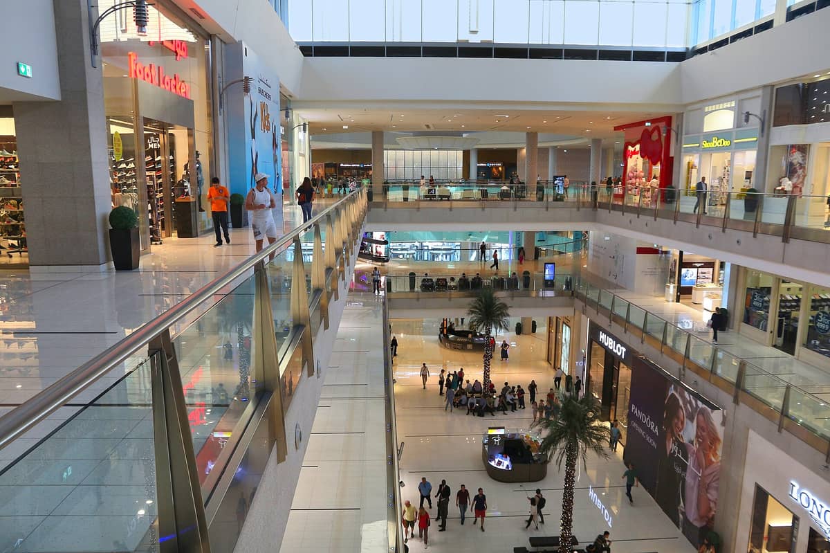 ภายใน Dubai Mall ที่แสดงให้เห็นหลายชั้น ร้านค้าหรูหรา นักช้อปที่กำลังเดินและกลุ่มคนที่มารวมตัว สะท้อนบรรยากาศการช้อปปิ้งที่คึกคักในช่วงฤดูท่องเที่ยว