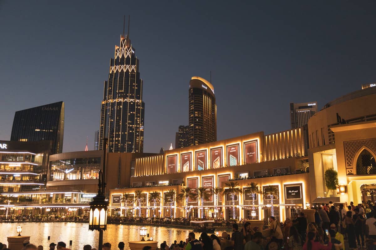 วิวยามเย็นของด้านนอก The Dubai Mall พร้อมตึกระฟ้าในเมืองและฝูงชนคึกคักริมน้ำ