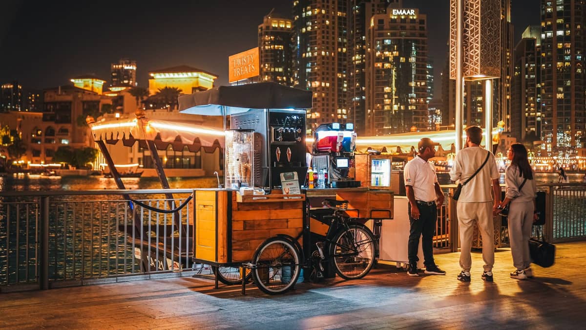 บรรยากาศยามค่ำคืนบนเส้นทางเดินริมน้ำ Dubai Marina พร้อมแผงอาหาร ผู้คน และตึกระฟ้าที่สว่างไสวอยู่เบื้องหลัง