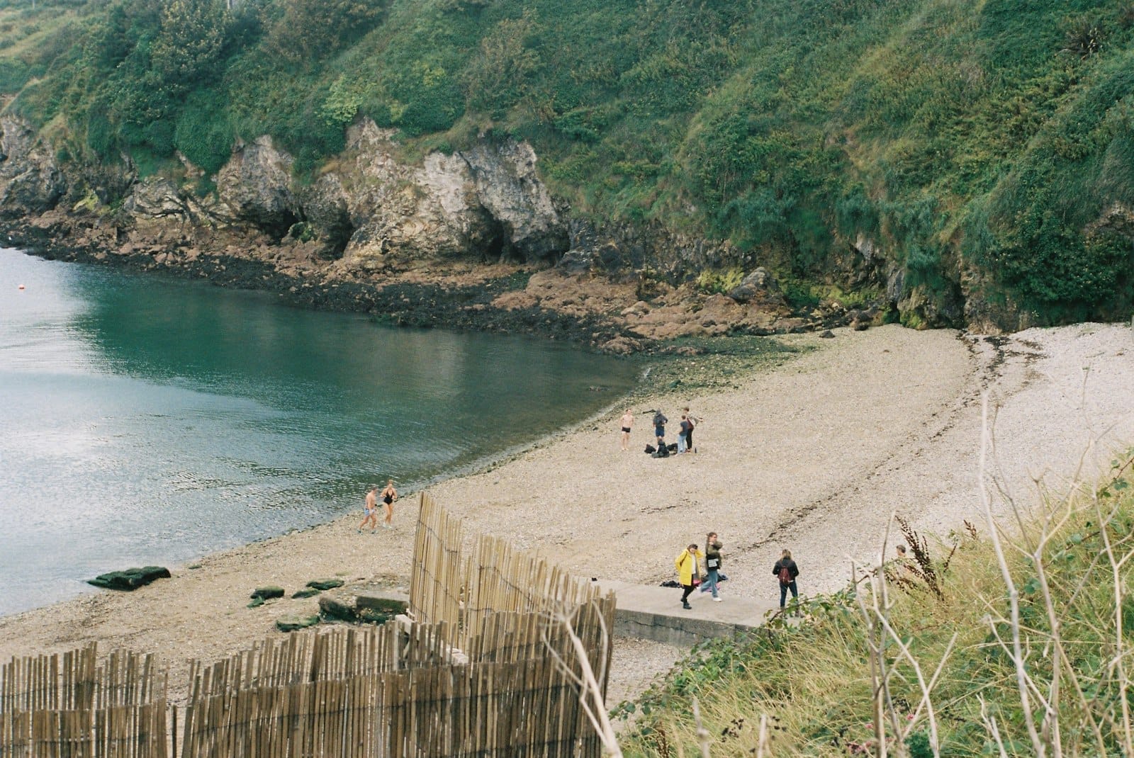 Uma pequena praia de areia abrigada, cercada por falésias rochosas e vegetação, com pessoas caminhando e curtindo a paisagem costeira perto de Dublin.