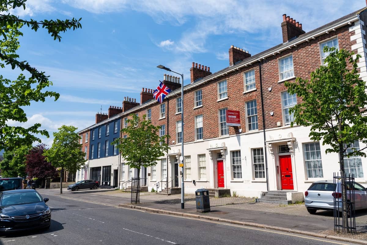Reihe klassischer georgianischer Stadthäuser mit roten Türen und Backsteingeländern auf einer sonnigen Straße im Zentrum von Dublin, Autos und Bäume sichtbar