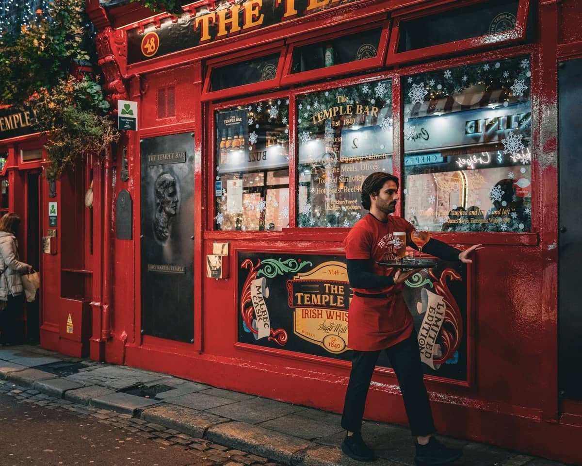 Kellner trägt Getränke vor dem Pub The Temple Bar in Dublin, einem berühmten Ort, bekannt für traditionelles irisches Essen und Trinken.