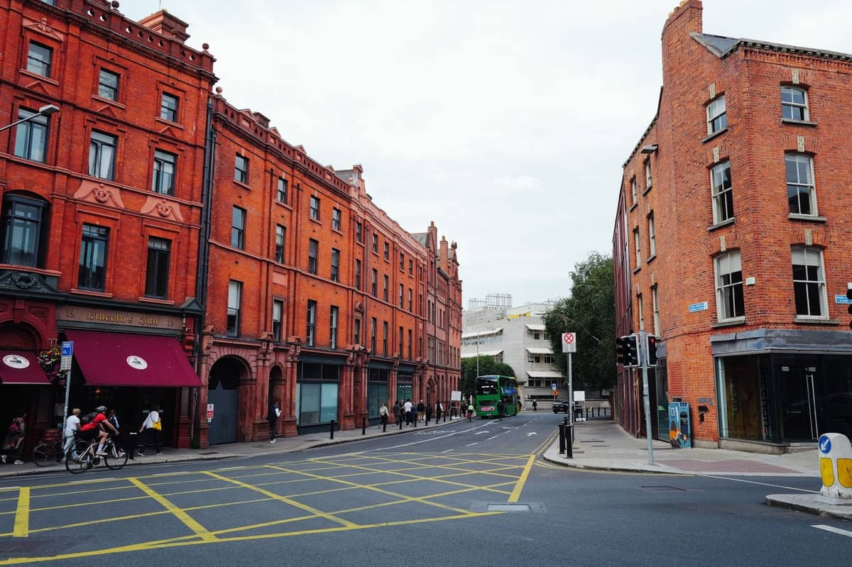 Breite Straßenansicht in Dublin mit georgianischen Backsteingebäuden, Cafés und leichtem Fuß- und Fahrradverkehr unter bewölktem Himmel.