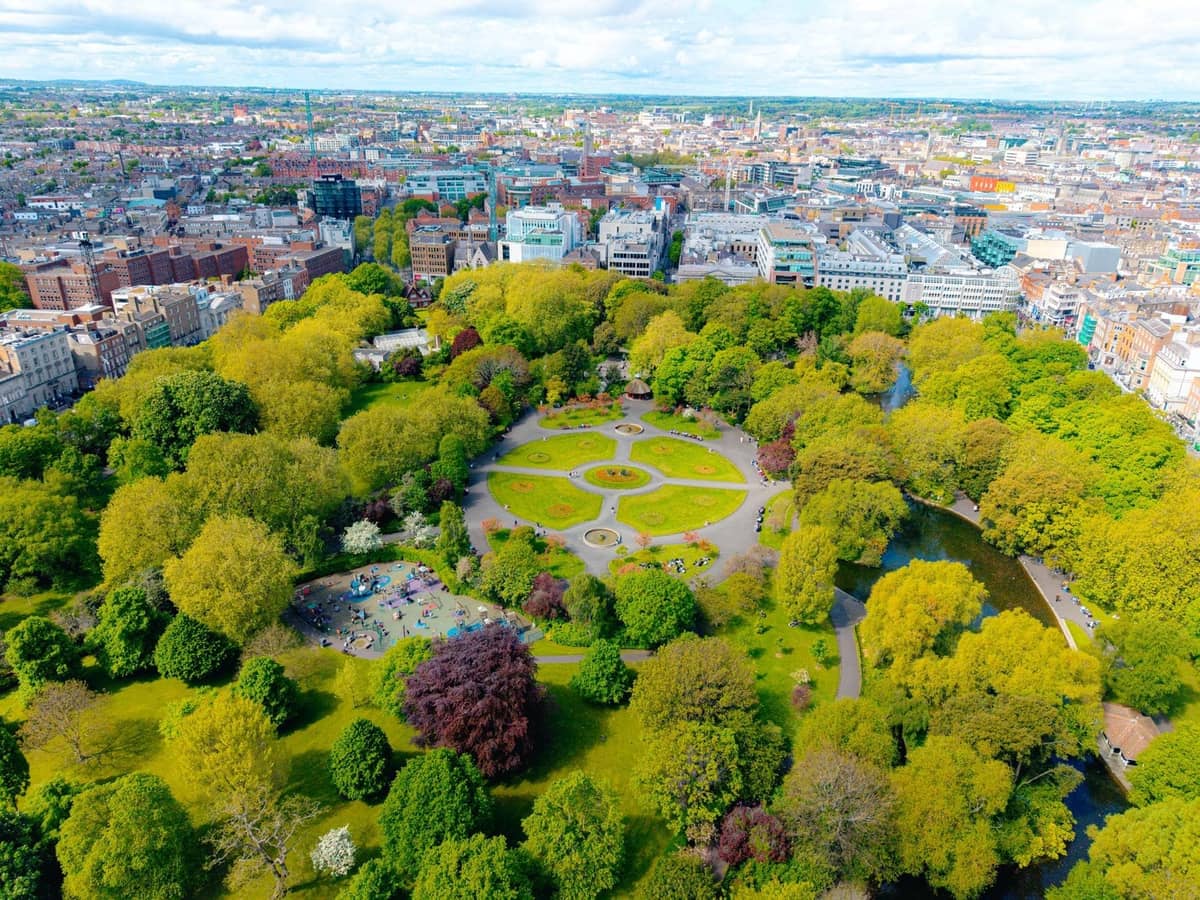 Vue aérienne d'un grand parc circulaire au centre de Dublin, rempli d'arbres luxuriants, de sentiers sinueux et de personnes se relaxant sur l'herbe.