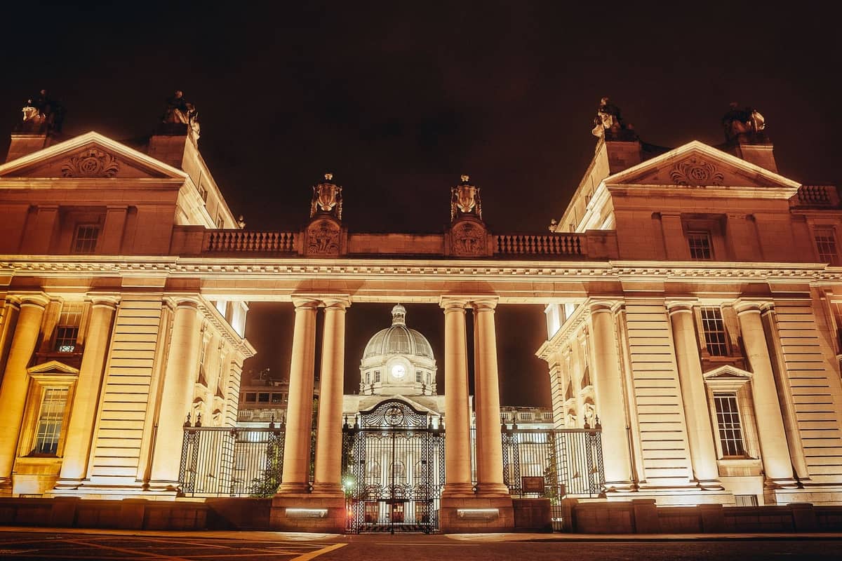Portails néoclassiques illuminés avec colonnes et bâtiment à dôme derrière, photographiés de nuit dans le centre-ville de Dublin.