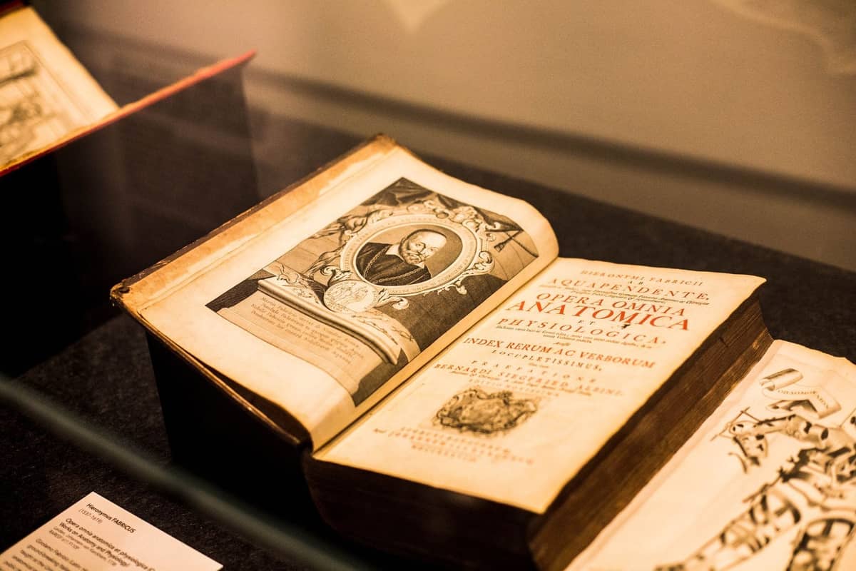 Ancien livre anatomique exposé dans une vitrine en verre, ouvert sur un portrait et des pages illustrées, dans un musée ou une exposition spéciale.