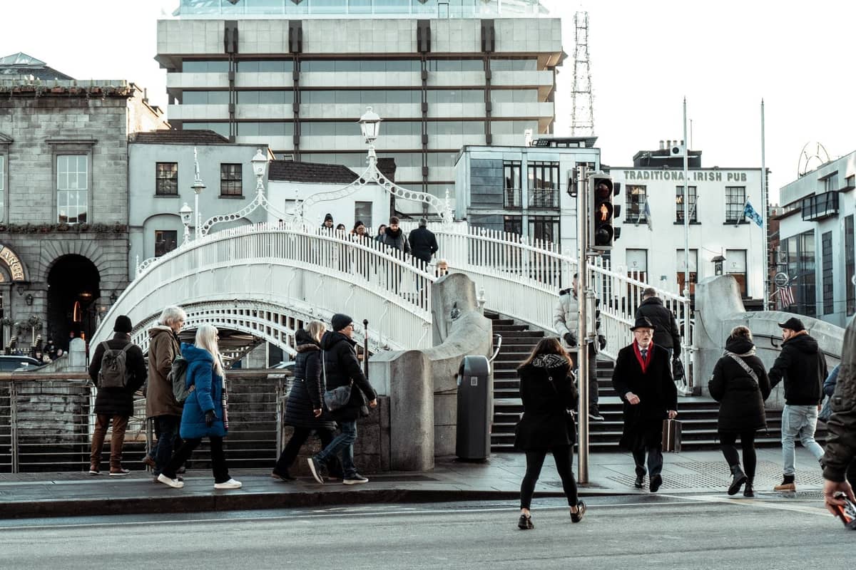 Des personnes en manteaux d'hiver traversent la rue près du célèbre Ha'penny Bridge à Dublin par une journée couverte.