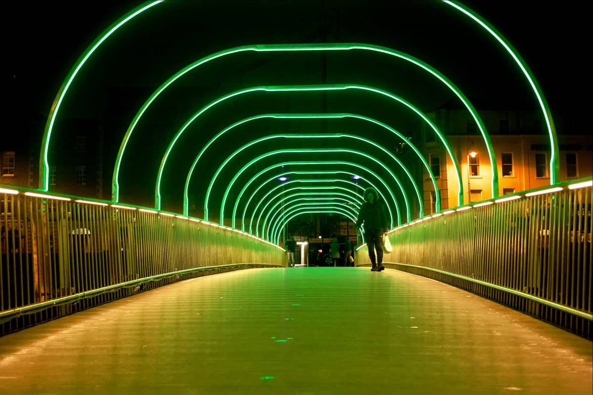 Personne marchant dans le tunnel d'un pont du centre-ville de Dublin illuminé par des arches festives de lumière verte vive la nuit.