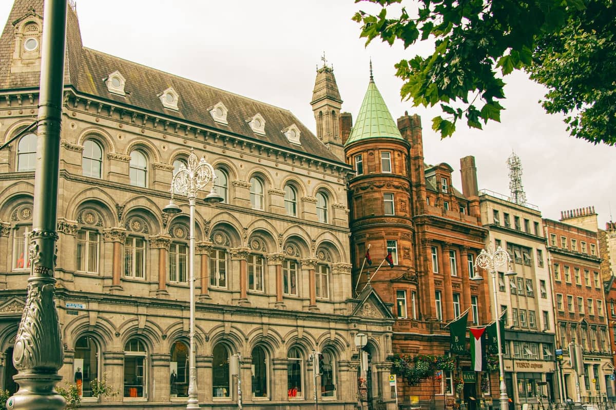 Elegante historische Gebäude entlang einer Straße in Dublin mit verzierten Fassaden und Laternen, belaubter Baum darüber, die Architektur des Stadtzentrums präsentierend.