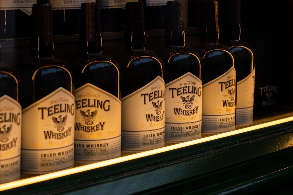 แถวขวด Teeling Irish Whiskey ที่วางแสดงบนชั้นวางในบาร์หรือโรงกลั่นที่มีแสงสลัว