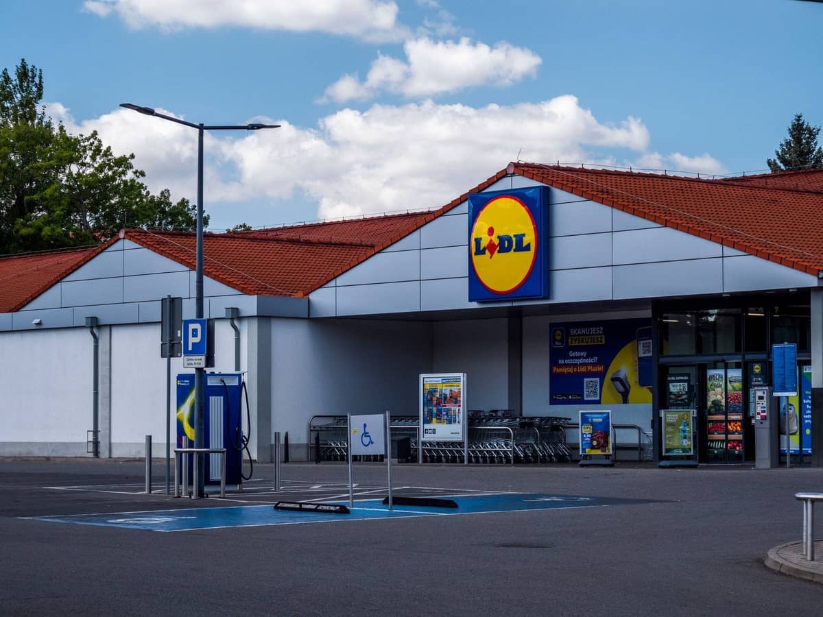 Außenansicht eines Lidl-Supermarkts mit Parkplätzen und Einkaufswagen draußen unter blauem Himmel.