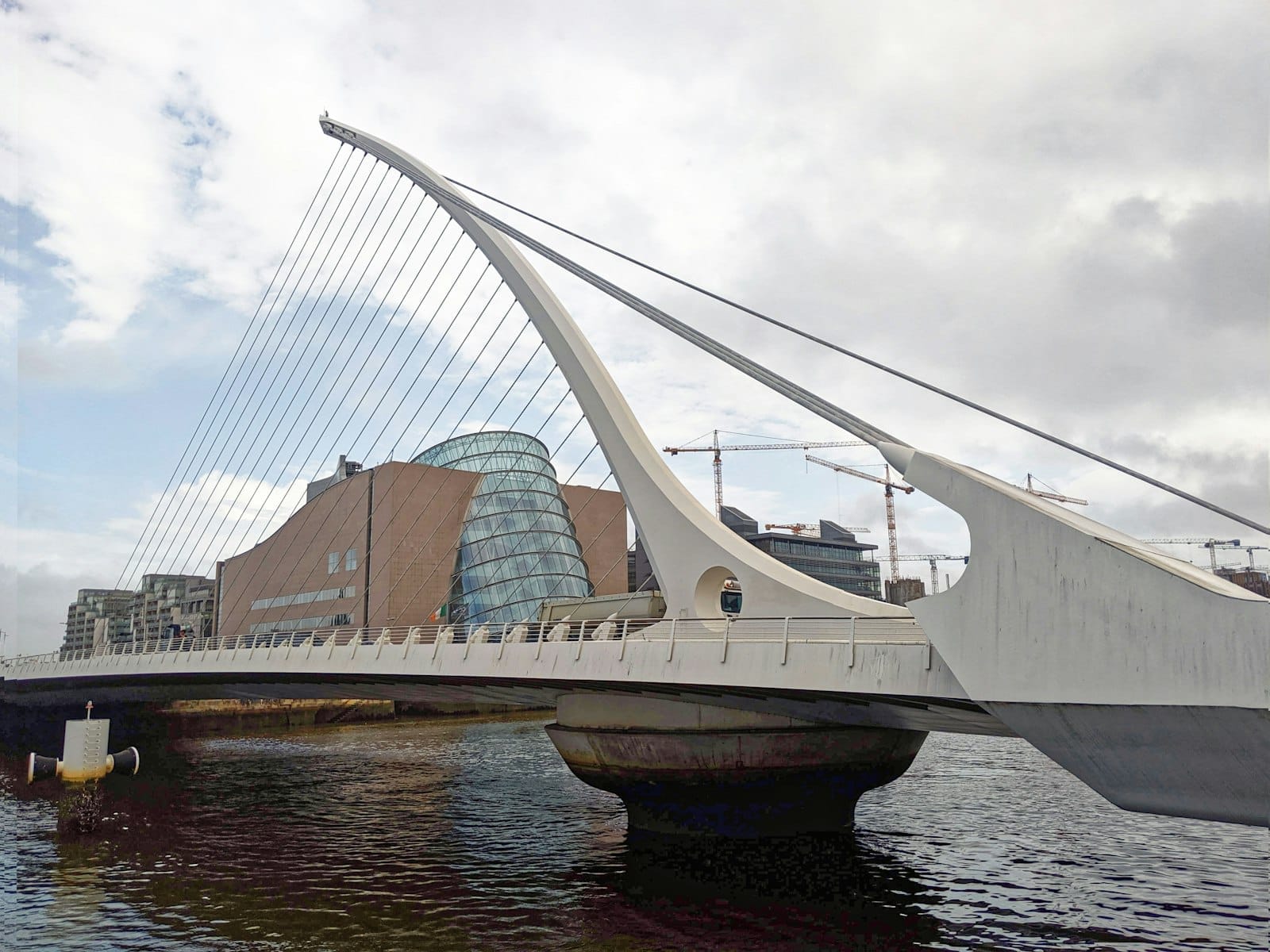Samuel Beckett Bridge spanning the River Liffey in Dublin, with the Convention Centre and modern cityscape in the background under cloudy skies.
