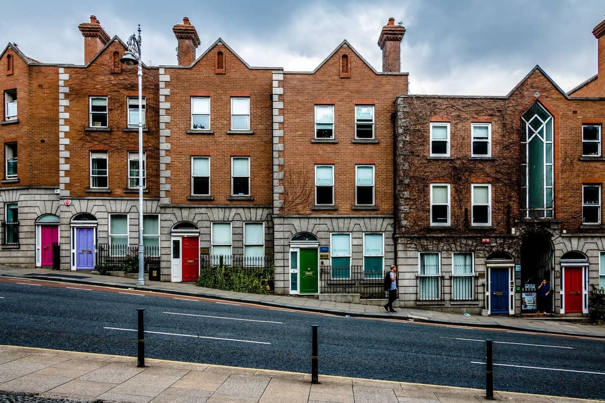 Una hilera de casas adosadas georgianas de ladrillo en Dublín, con puertas delanteras de colores y ventanas en arco a lo largo de una calle ligeramente empinada.